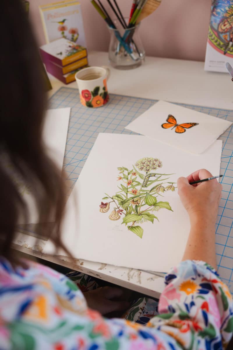 Photo from behind Erin as she adds color to an illustration of a caterpillar on a plant