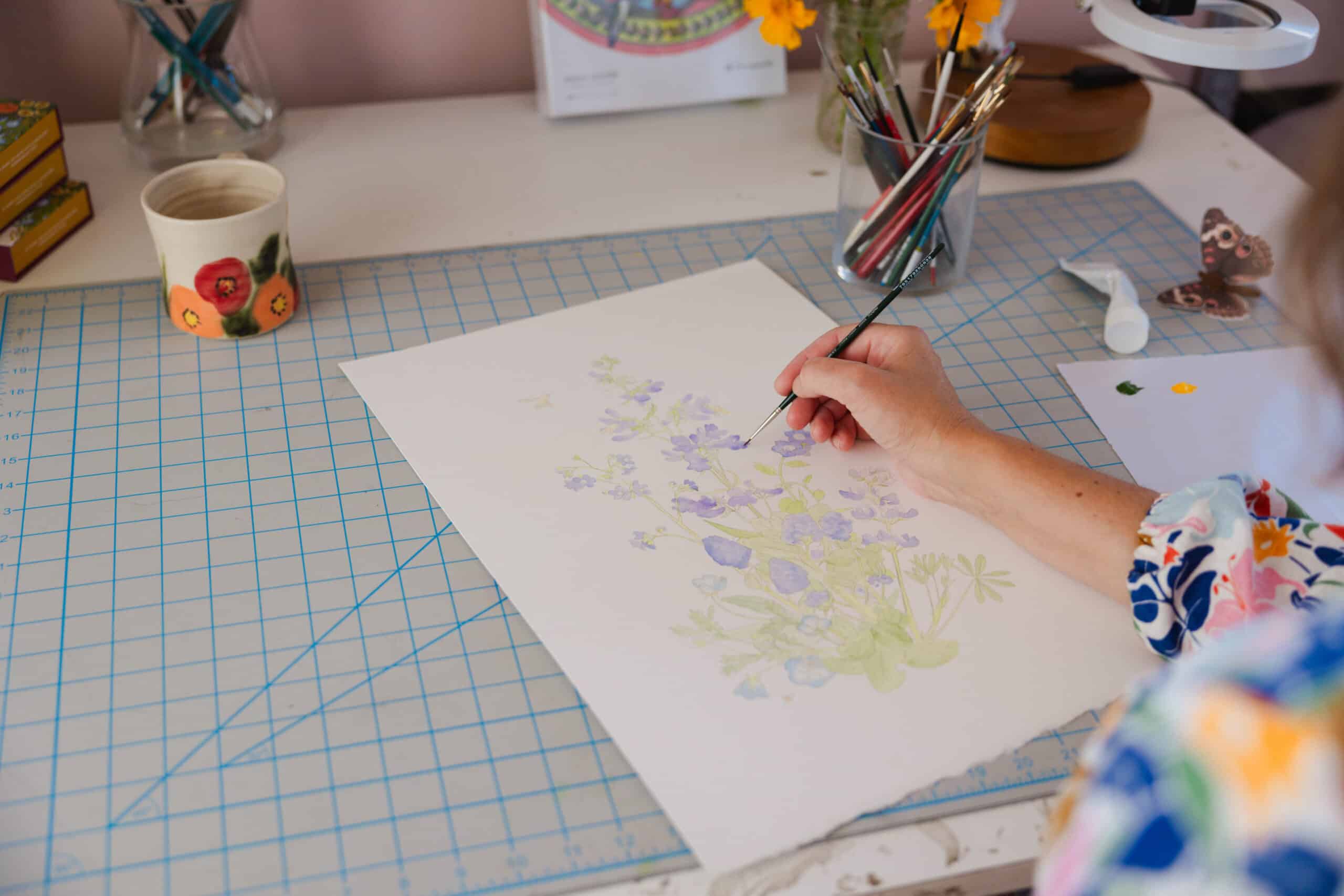 Image of Erin sitting at her drafting table, painting a botanical illustration